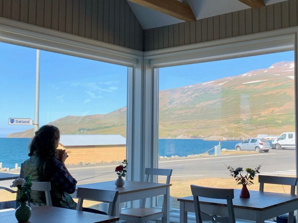 A woman sips a cup of tea while looking out the window at the mountains and sea from the dining room at Grenivik Guesthouse.