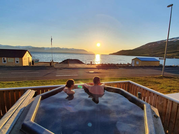 People relax in the outdoor hot tub at Grenivik Guesthouse and look out over Eyjafjordur fjord.
