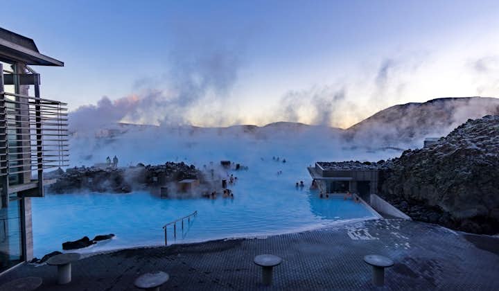 People bathing in the Blue Lagoon geothermal spa amid a natural landscape with steam rising into the air.