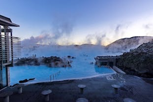 People bathing in the Blue Lagoon geothermal spa amid a natural landscape with steam rising into the air.