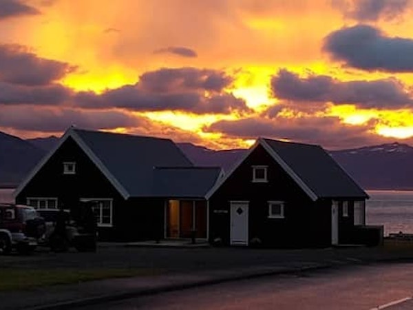 Exterior view of Grenivik Guesthouse on a cloudy day at sunset with pinks and yellows lighting up the sky.