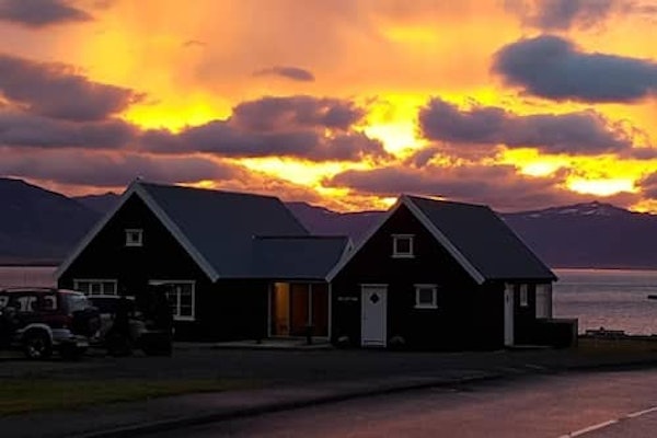 Exterior view of Grenivik Guesthouse on a cloudy day at sunset with pinks and yellows lighting up the sky.