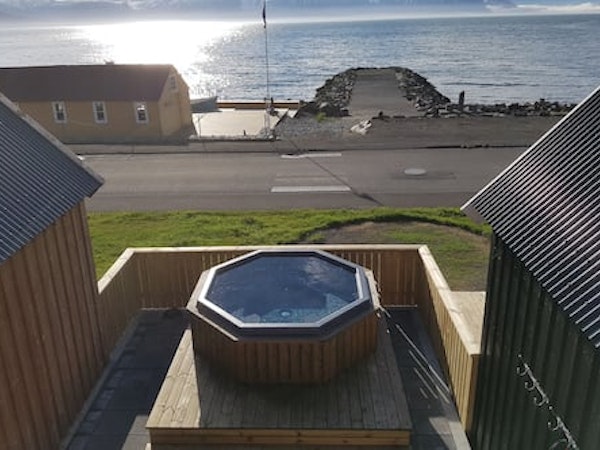 An overhead view of the outdoor hot tub at Grenivik Guesthouse with the patio surrounding, and the road and fjord in front.