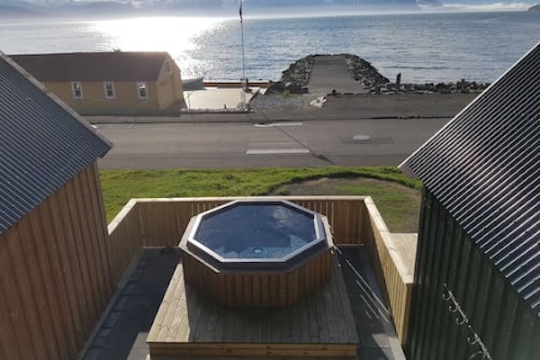 An overhead view of the outdoor hot tub at Grenivik Guesthouse with the patio surrounding, and the road and fjord in front.