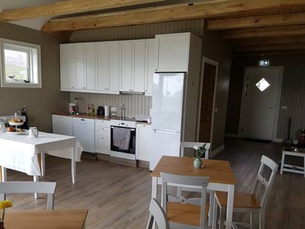 The open-plan kitchen and dining area at Grenivik Guesthouse with tables, chairs, and an oven in the kitchen.