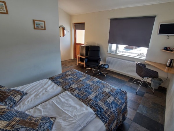 View of a double room at Fossatun Country Hotel with a bed, comfortable chair, and desk.
