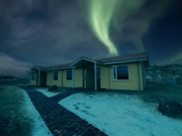 Exterior view of Fossatun Country Hotel with snow on the ground at night time and the green colors from the aurora borealis ligh