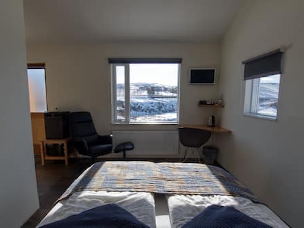 View of a double room at Fossatun Country Hotel with a bed, comfortable chair, and desk, and a nature view outside the window.