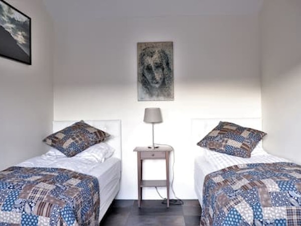 A twin bedroom at Fossatun Country Hotel with a bedside table, lamp, and a picture on the wall.