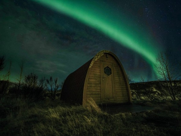A bright green streak from the aurora borealis in the sky above one of the Fossatun camping pods with a rounded roof.