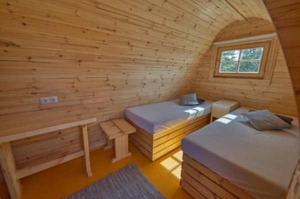 Beds, tables, and the wooden interior of a rounded-roof Fossatun camping pod.