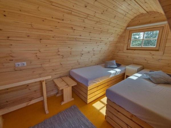 Beds, tables, and the wooden interior of a rounded-roof Fossatun camping pod.