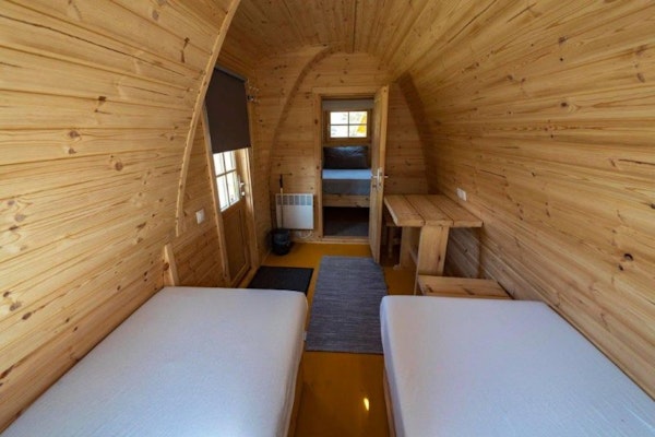 Twin beds, tables, and the wooden interior of a rounded-roof Fossatun camping pod.