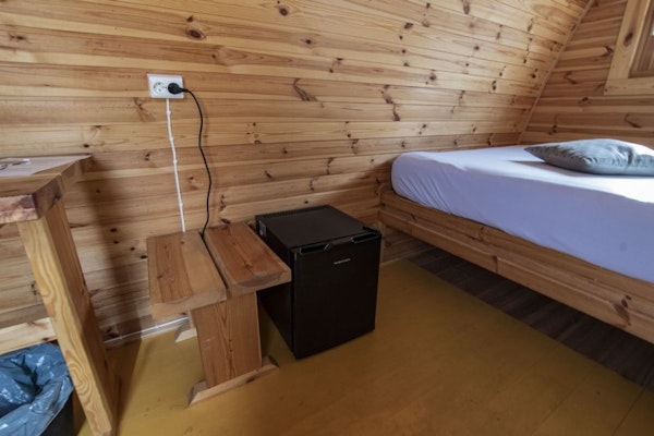 A bed and table with a socket above it inside a Fossatun camping pod.