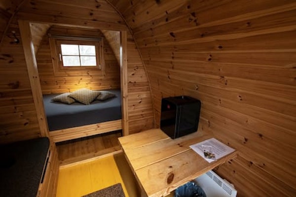 A bed, table, and the wooden interior of a Fossatun camping pod.