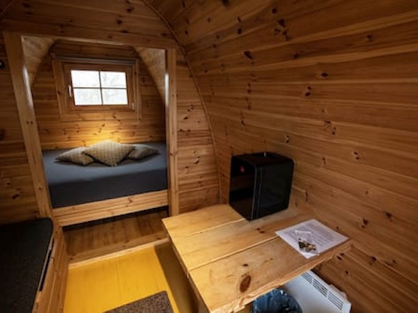 A bed, table, and the wooden interior of a Fossatun camping pod.