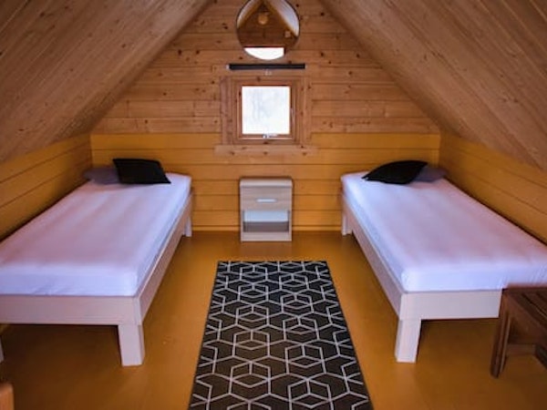 Twin beds, and the wooden interior of a pointed-roof Fossatun camping pod.