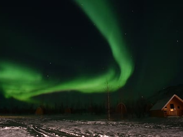 A bright green streak from the aurora borealis lights up the night sky above Fossatun camping pods.