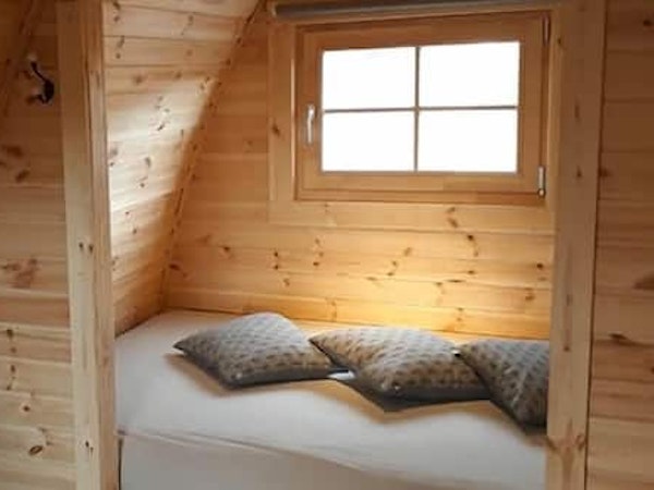 A bed with cushions and a window above inside a Fossatun camping pod.
