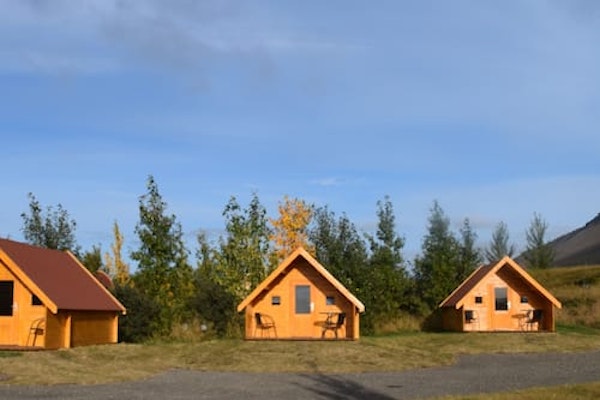 The Fossatun camping pods with a pointed-roof style amid green trees with a blue sky above.