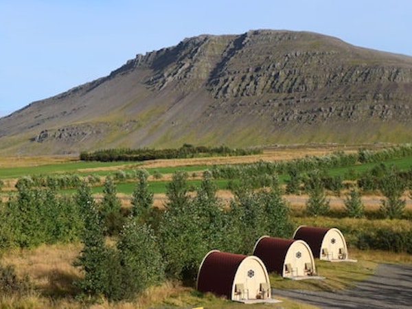 An overhead landscape view of some of the Fossatun camping pods with greenery surrounding and a hill beyond.