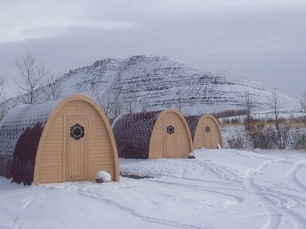 Three of the Fossatun camping pods with a rounded roof amid a snowy landscape with a hill beyond.