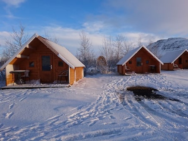 The Fossatun camping pods with a pointed-roof style amid a snowy landscape on a blue-sky day.