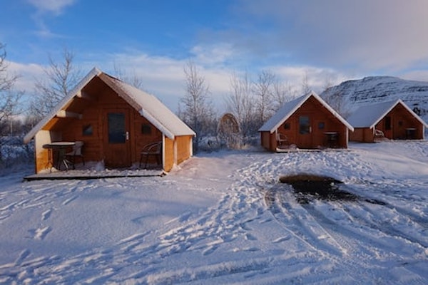 The Fossatun camping pods with a pointed-roof style amid a snowy landscape on a blue-sky day.