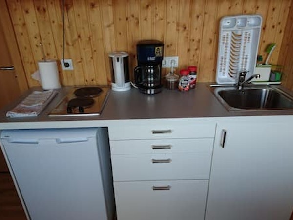 A close-up view of the bench area in the Fossatun Sunset Cottage with a fridge, coffee maker, kettle, tea, coffee, and sink.