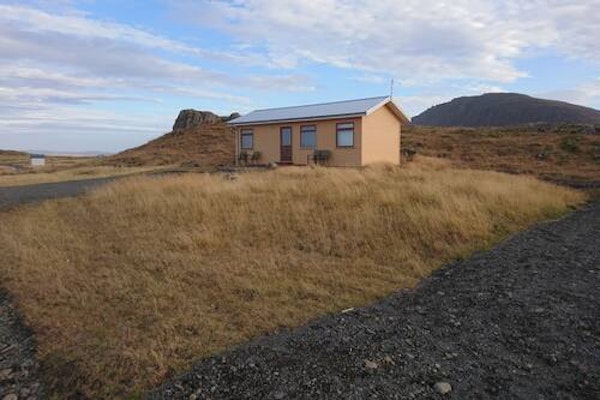 Front exterior view of Fossatun Sunset Cottage with a grassy surrounding landscape and hills behind.