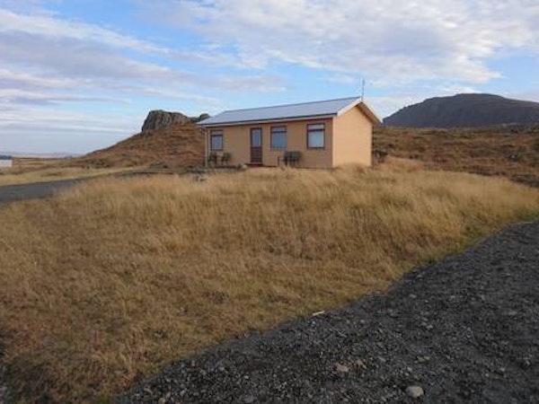 Front exterior view of Fossatun Sunset Cottage with a grassy surrounding landscape and hills behind.