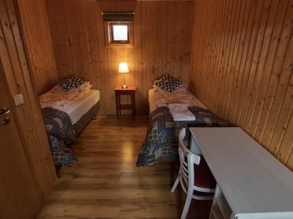 Two single beds with towels, a bedside table and lamp, and a desk and chair in a room at Fossatun Sunset Cottage.