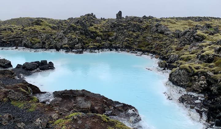 The milky blue water of the Blue Lagoon geothermal spa is surrounded by a rugged, rocky landscape.