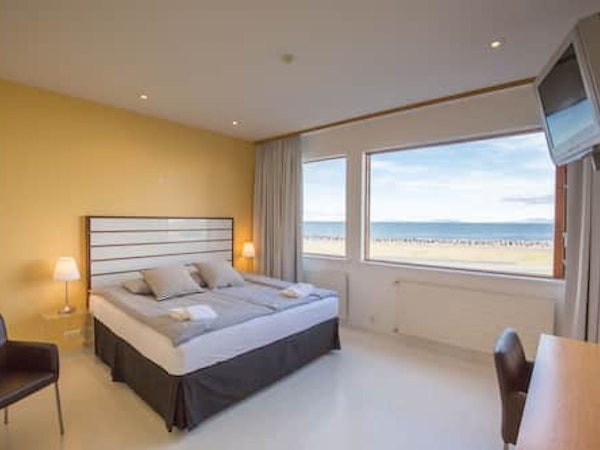A deluxe room with a large bed, lamp, towels, and a sea view at Hotel Keilir.