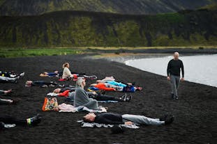 A group of people on a black sand beach in Iceland, lying on towels. Some are lying down, some are sat up.