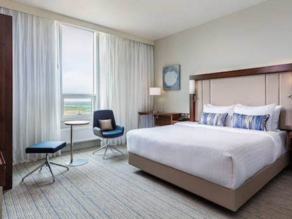 A room with a king bed, comfortable chair, and large windows at the Courtyard by Marriott Reykjavik Keflavik Airport.