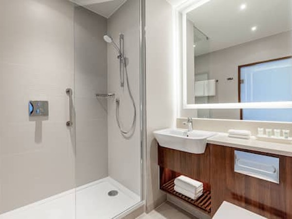 A bathroom with a shower, basin, mirror, and towels at the Courtyard by Marriott Reykjavik Keflavik Airport.