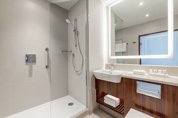 A bathroom with a shower, basin, mirror, and towels at the Courtyard by Marriott Reykjavik Keflavik Airport.
