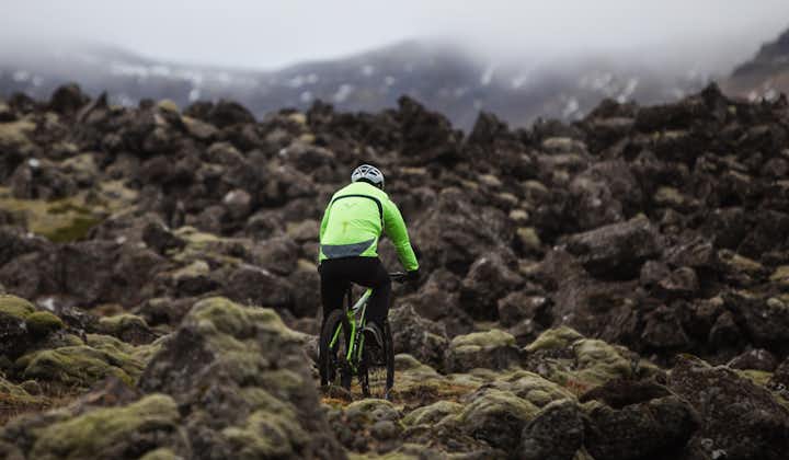 Een man in een waterbestendige jas rijdt op een mountainbike over de rotsen.