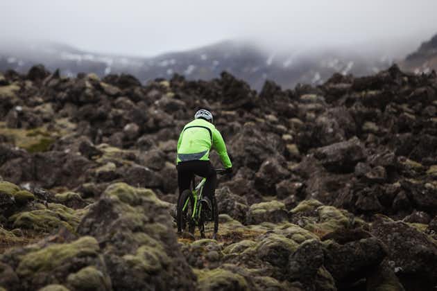 Mann mit wasserdichtem Mantel, der mit dem Mountainbike über Felsen fährt.