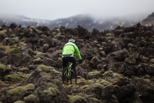 Велосипедист в непромокаемой куртке едет на горном велосипеде по камням.