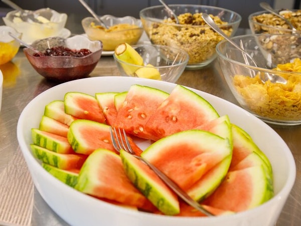 A plate of freshly cut watermelon and bowls of cereals and jams behind it in the buffet area at Hotel Laugar Reykjadalur.