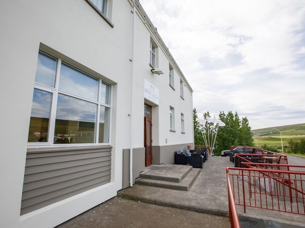 An exterior view of Hotel Laugar Reykjadalur with outdoor furniture and a parking area.