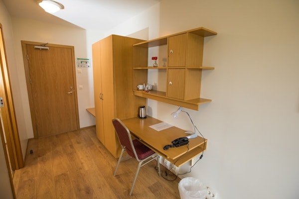 A desk, chair, trash can, kettle, telephone, closet, shelving, and cupboards in a room at Hotel Laugar Reykjadalur.