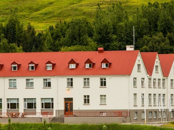 Exterior view of Hotel Laugar Reykjadalur with its striking red roof contrasting with the green trees and hills behind.