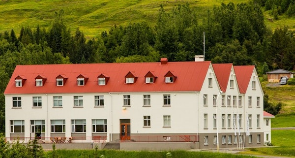 Exterior view of Hotel Laugar Reykjadalur with its striking red roof contrasting with the green trees and hills behind.