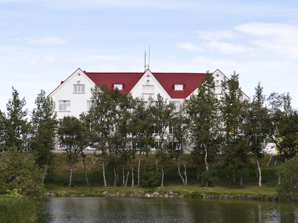 A small lake lined with trees in front of Hotel Laugar Reykjadalur.