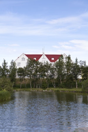 A small lake lined with trees in front of Hotel Laugar Reykjadalur.