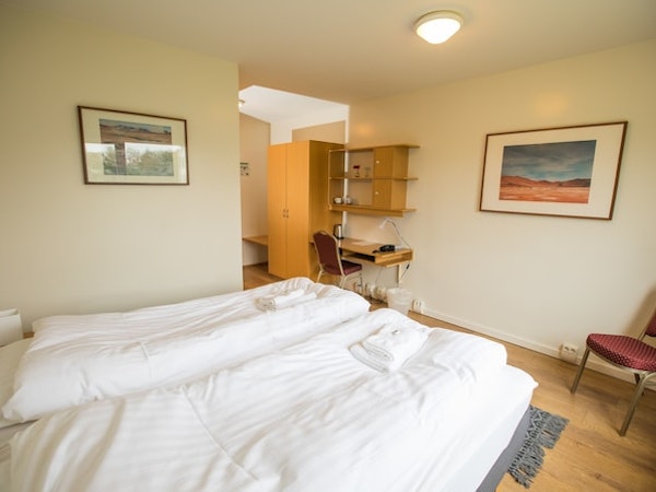 A double bedroom with a desk, chair, closet, towels, and shelving at Hotel Laugar Reykjadalur.