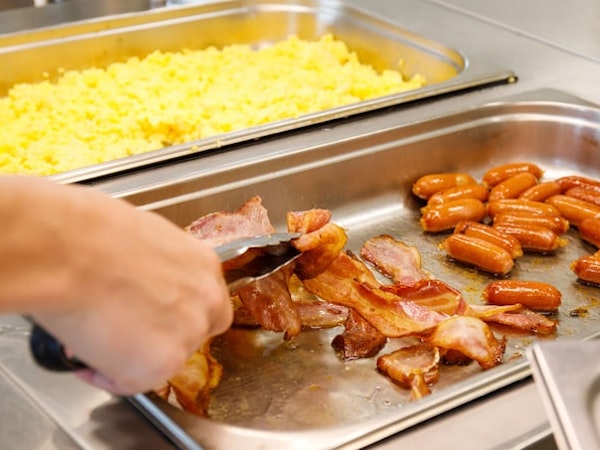 A person is selecting bacon from the breakfast buffet area, which also included sausages and scrambled eggs at Hotel Laugar Reyk